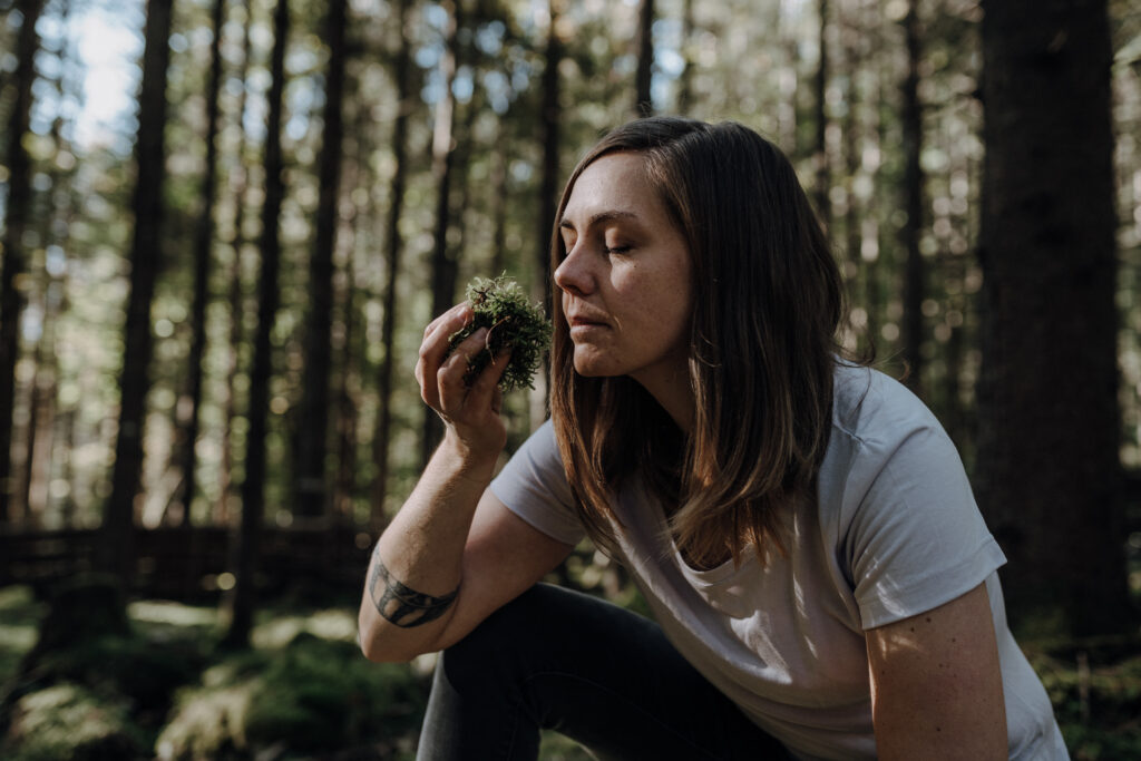 Franziska riecht an einem Moss im Wald, mit geschlossenen Augen. 